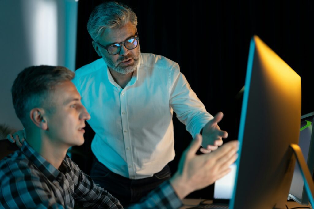 Mentor sênior orientando funcionário no escritório durante sessão de trabalho noturna