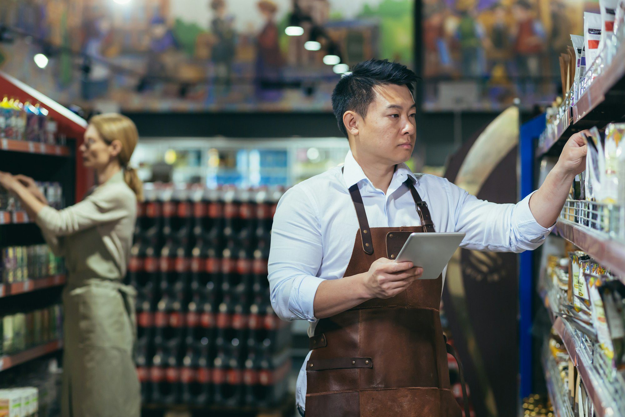 dois trabalhadores em um supermercado no departamento de mercearia organizam produtos um homem asiático com tablet